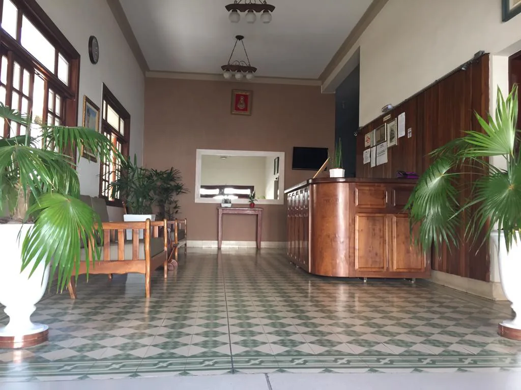 Recepção do Hotel Internacional, com piso xadrez, plantas e balcão de madeira